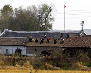 A group of DPRK residents fix tiles on the roof of a house yesterday across the Yalu River.