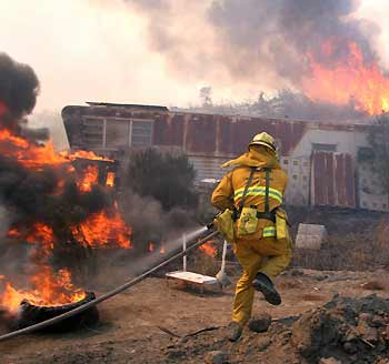 Los Angeles firefighter Brent Roff rushes to stop flames from burning a mobile home in the West Hills area of Los Angeles September 29, 2005. Thick smoke hung over much of Los Angeles on Thursday as a wildfire burned out of control in the Southern California foothills, threatening upscale suburban neighborhoods as firefighters struggled to keep the flames from racing to the sea. [Reuters]