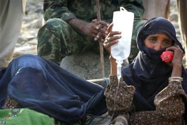 An earthquake survivor holds an IV bag for a loved one as they wait for a helicopter to arrive and evacuate them from a river bank in Balakot, Pakistan Thursday, Oct. 13, 2005.