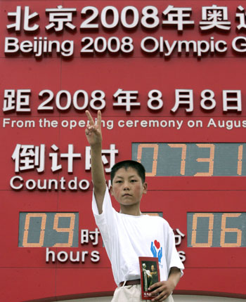 A boy, holding a picture of the late Chairman Mao Zedong, shows a "V" sign in front of a huge Beijing 2008 Olympic Games countdown clock in Beijing August 8, 2006. Sports and cultural activities were held around the capital to mark the two-year countdown to the 2008 Olympic Games in Beijing.
